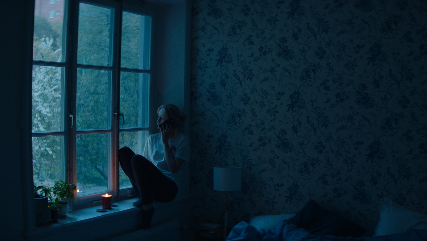 a woman sits on the window sill of a bedroom at night talkin 62885ea99a0df68c4034e283bb965448