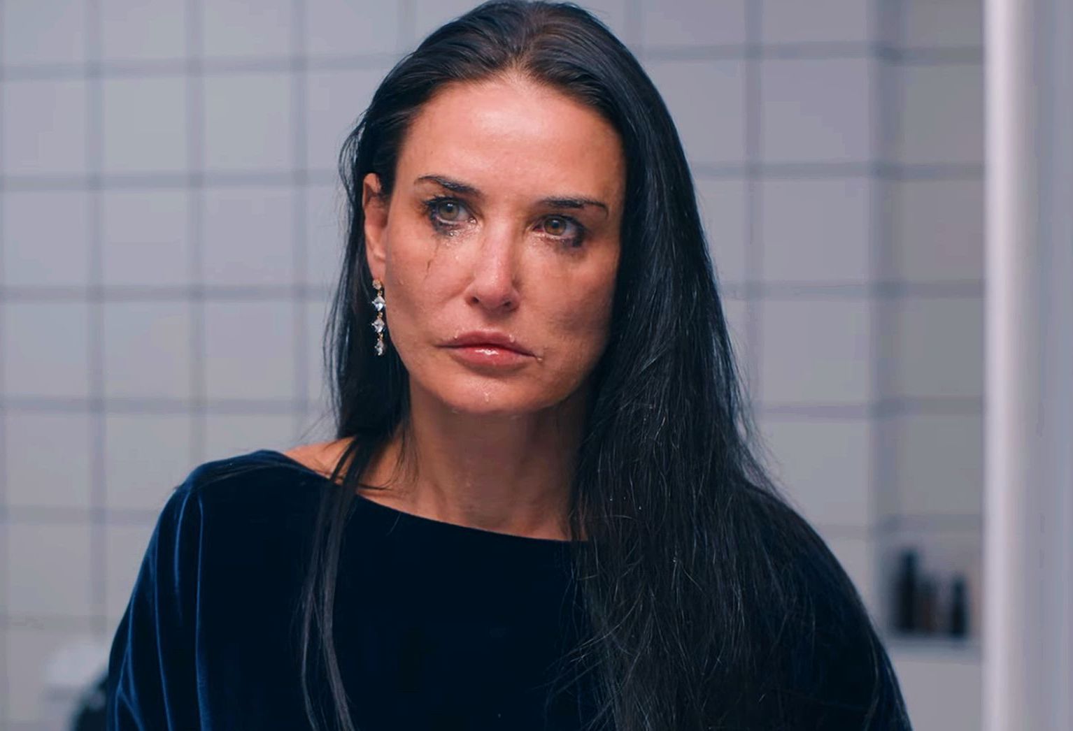 demi moore grimmacing in the mirror of a white tiled bathroom in the substance